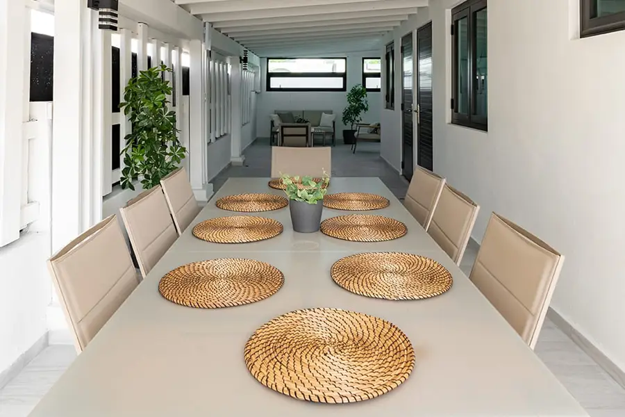 A long table with wicker placemats on it set for a meal.