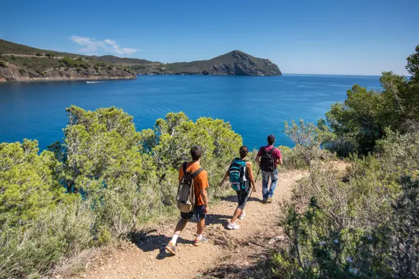 Three hikers walking along a coastal trail with a scenic view of the ocean and an island in the distance.